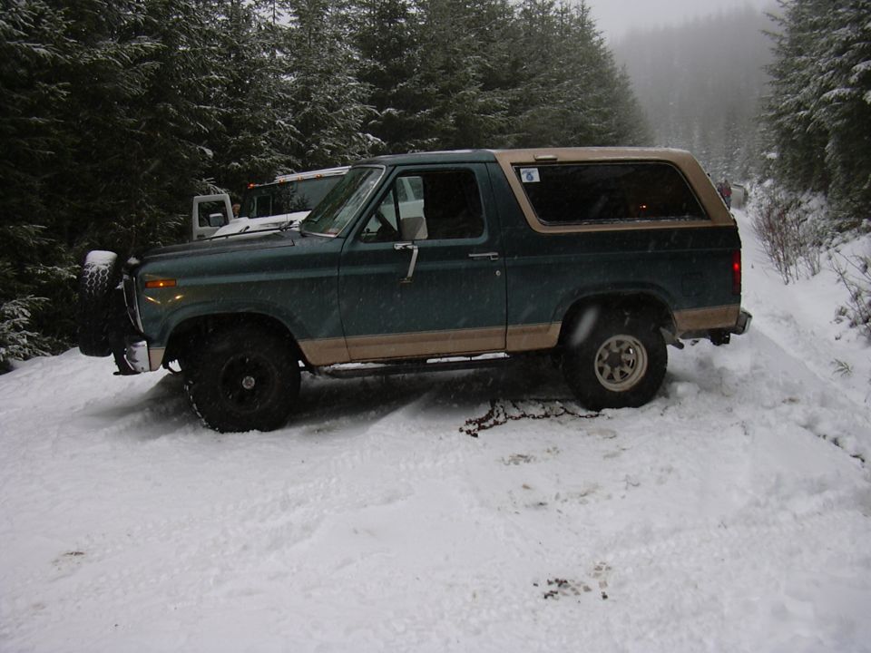 Green and tan Ford Bronco with a spare tire mounted on the front, parked in snow