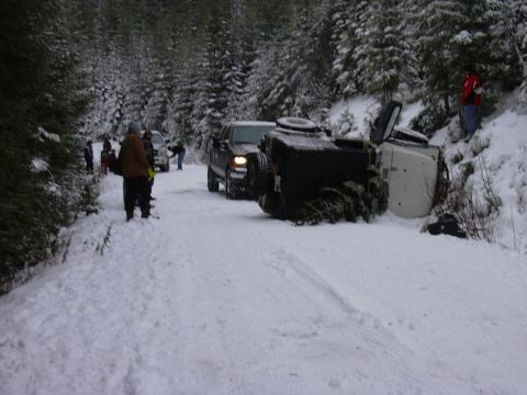 1991 Ford Bronco - Multiple vehicles are present on a snow-covered road, with one vehicle overturned.