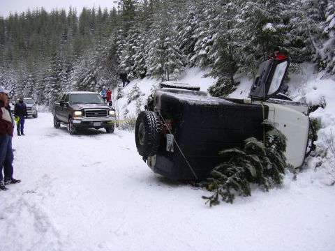 1991 Ford Bronco - A pickup truck tows an overturned SUV out of a snowy ditch, with trees lining the background.