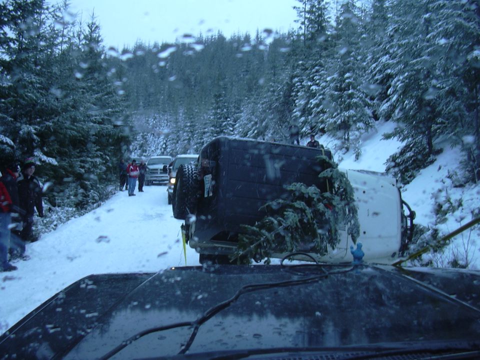 overturned vehicle on snowy road with trees and people around