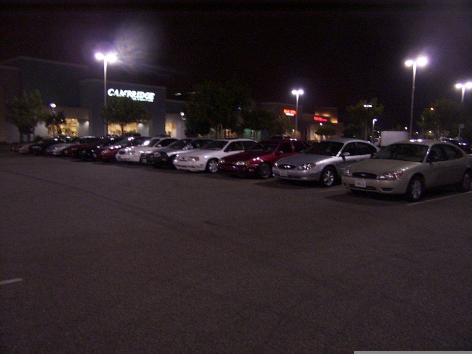 Several sedans parked in a lot at night, with a building in the background