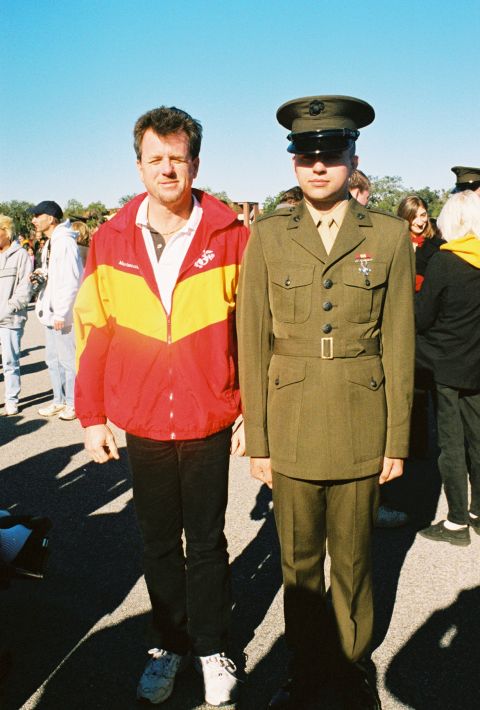 1994 Ford Bronco - A man in a military uniform stands next to a man wearing a red and yellow jacket, with other people in the background.