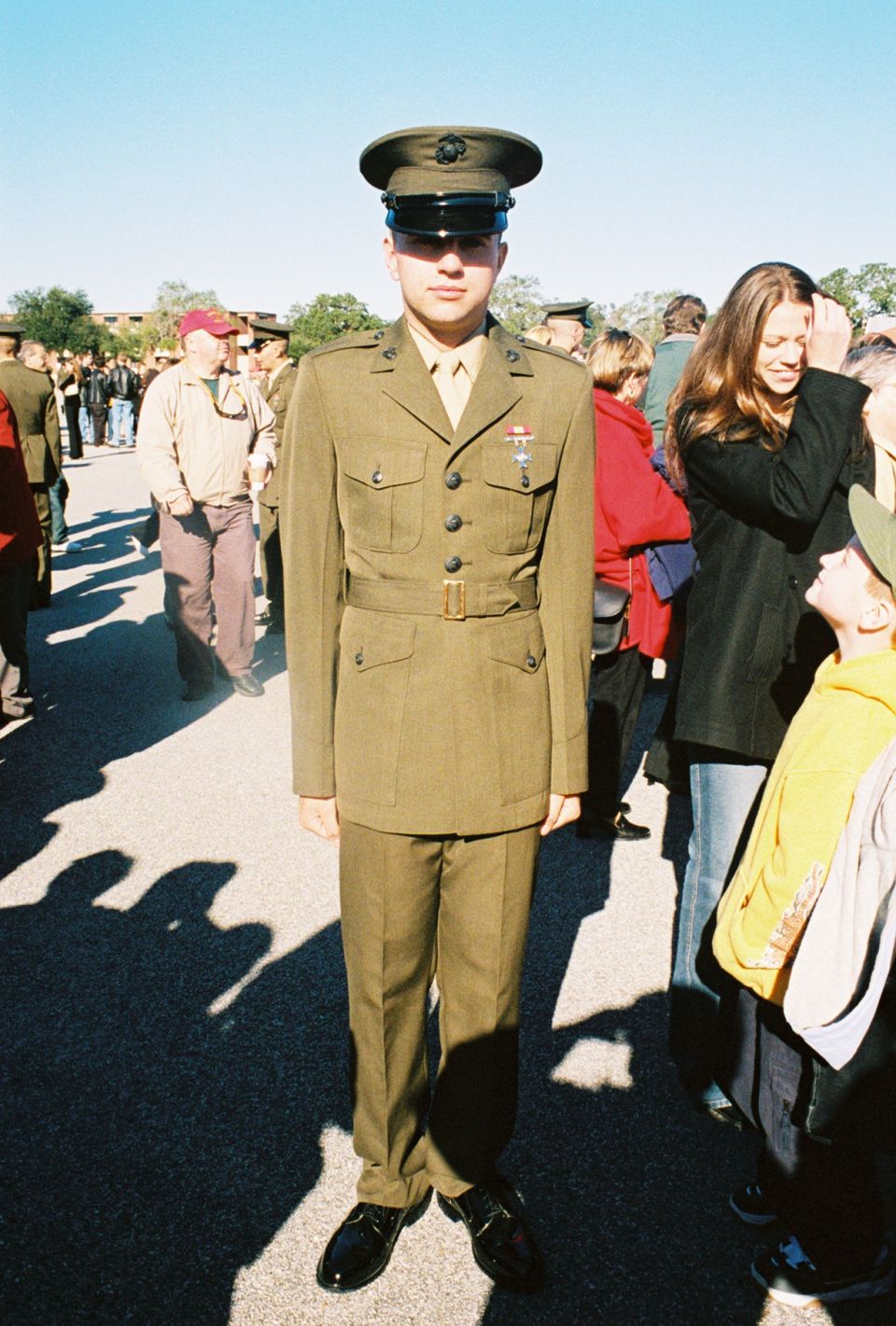 US Marine in dress uniform standing outdoors with civilians in the background