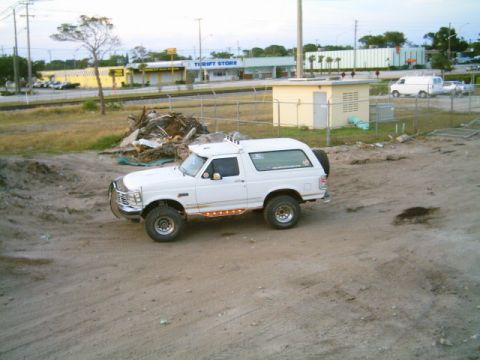 1995 Ford Bronco - White lifted full-size Ford Bronco parked on a sandy vacant lot, shown from an elevated driver's-side front three-quarter angle. It carries…