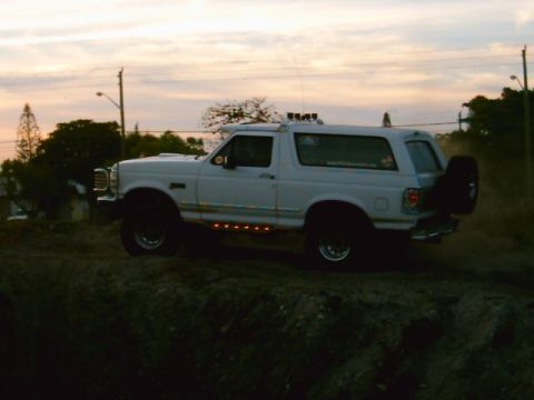 1995 Ford Bronco - This SUV is seen from the side, driving on a dirt path during dusk.