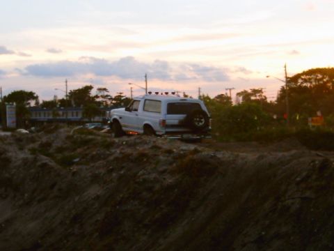 1995 Ford Bronco - Silhouetted dusk shot of a white lifted Ford Bronco parked on a dirt berm, seen from the passenger side with its roof light bar and amber r…