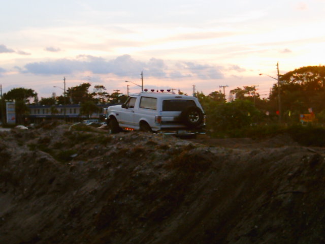 White lifted Ford Bronco on a dirt berm at sunset with roof lights lit
