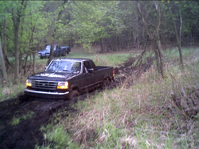 1995 Ford F-150 stuck in mud with another truck behind it in woods