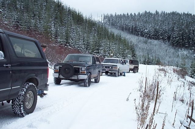 Black Ford Bronco with spare tire on front, in a snowy forest