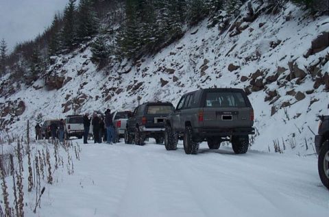 1995 Ford Bronco - Multiple SUVs are parked in a line on a snowy mountain road during an event.