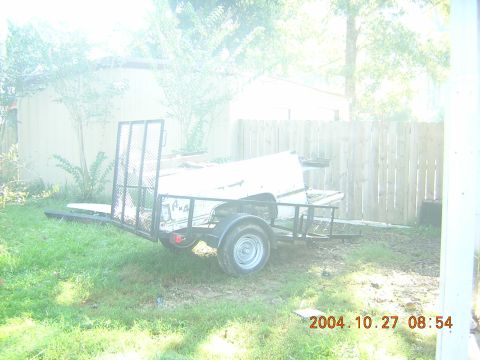 1984 Chevrolet Blazer - A trailer sits in a grassy yard next to a wooden fence, with a white object loaded on top.