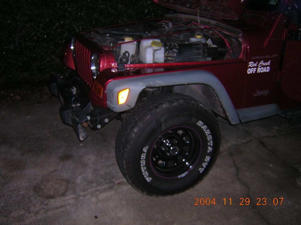Front corner of red Jeep Wrangler, hood open, showing engine bay. "Red Creek OFF ROAD" sticker on fender