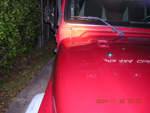1984 Chevrolet Blazer - Close-up of a red Jeep Wrangler's hood and fender, showing the side mirror and text on the hood.