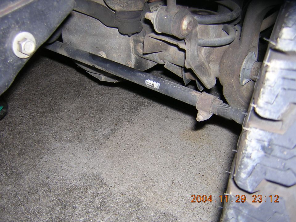 Close-up of vehicle's rear suspension and tire, showing a metal bar and coil spring