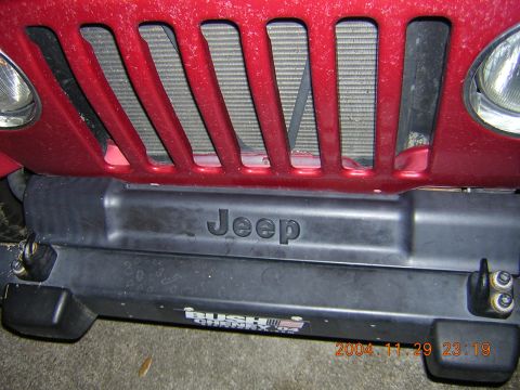 1984 Chevrolet Blazer - Close-up of a red Jeep's front grille and bumper, showing the embossed 'Jeep' logo.