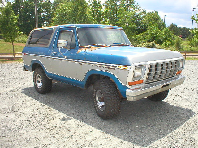 Blue and silver Ford Bronco parked on gravel. It has a silver grille and chrome bumper