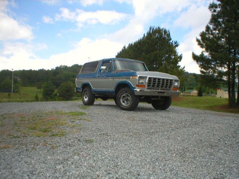 1978 Ford Bronco - A blue and silver 1978 Ford Bronco sits on a gravel surface under a cloudy sky.