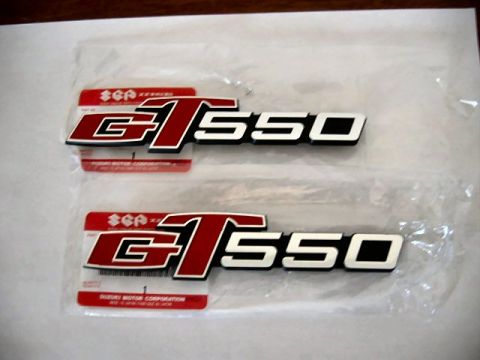 1985 Ford LTD Crown Victoria - Two new Suzuki GT550 side cover emblems in red and white lettering, still attached to Suzuki Motor Corporation parts labels.