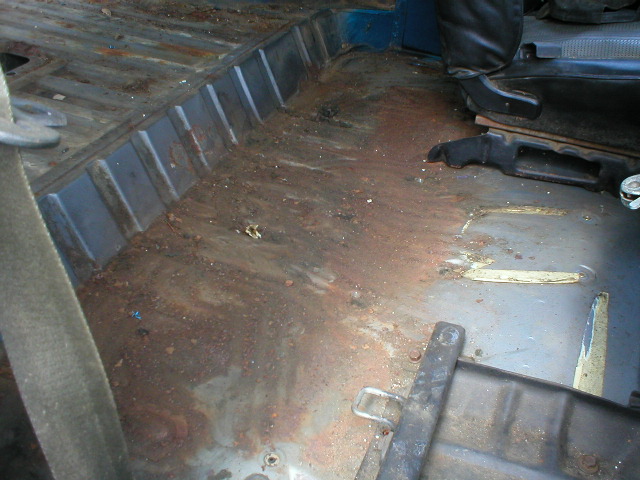 Stripped vehicle interior floor pan showing surface rust with carpet and trim removed