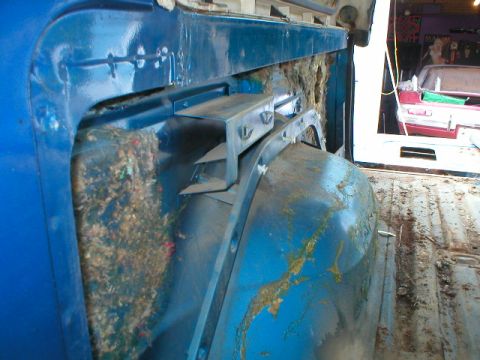 1978 Ford Bronco - Stripped interior rear quarter and wheel tub of a blue truck body, with dried mud and grass debris packed behind the inner panel and streak…