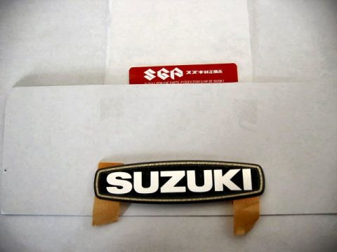 1985 Ford LTD Crown Victoria - Suzuki emblem and a red label indicating Suzuki Genuine Parts are shown against a white surface.