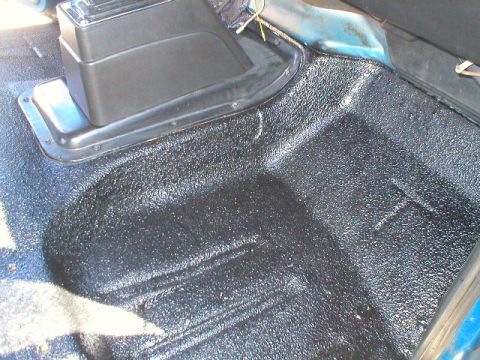 1978 Ford Bronco - Interior floor of a vehicle freshly coated with black textured bedliner (Herculiner), showing the transmission tunnel hump and center conso…