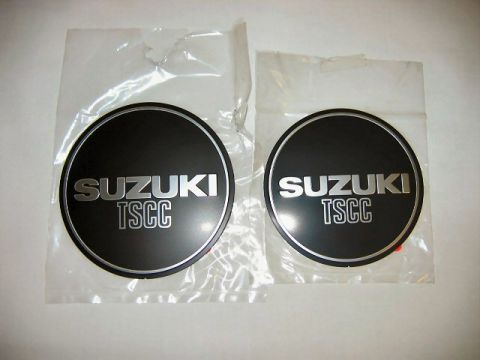1985 Ford LTD Crown Victoria - Pair of round Suzuki TSCC badges with silver lettering on black, sealed in clear plastic packaging.