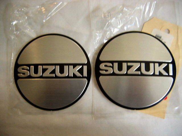Two circular Suzuki emblems with silver brushed metal finish and black trim