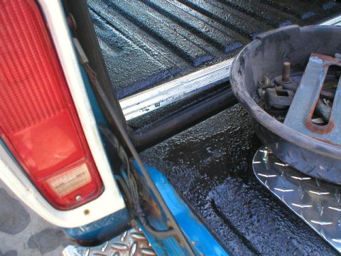 1978 Ford Bronco - Close-up of a truck bed and tailgate area freshly coated with black Herculiner-style bedliner, showing the textured wet-look surface. A red…