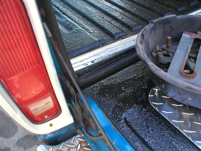 Truck bed with fresh black textured bedliner coating, red taillight and diamond plate at left