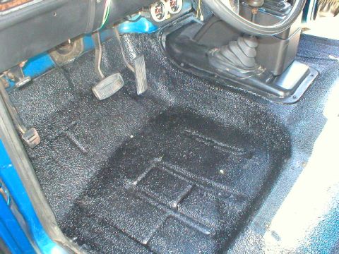 1978 Ford Bronco - The interior floor of an early Bronco freshly coated in black textured bedliner, showing the brake and clutch pedals, a floor-mounted shift…