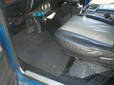 1978 Ford Bronco - Interior driver's side floor of a 1978 Ford Bronco showing black rubber floor mats over dark carpet, a black bench/bucket seat with gray in…