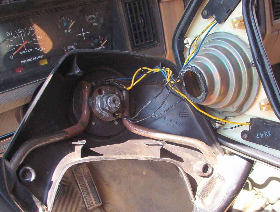 Steering wheel removed exposing column hub and gauge cluster, yellow and blue wires hanging loose