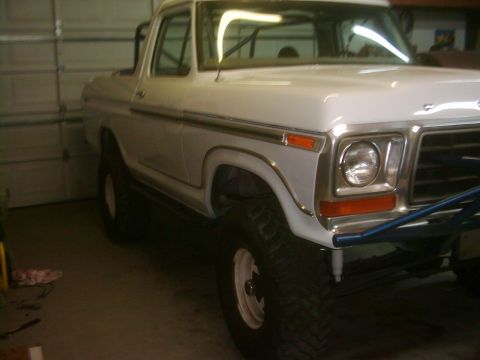 1978 Ford Bronco - This 1978 Ford Bronco features off-road tires and a custom blue front bumper, seen parked indoors.