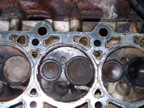 1996 Ford Crown Victoria - Close-up of a used engine cylinder head showing wear and tear on the valves and surrounding metal.