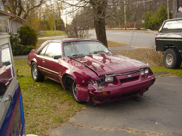 Maroon Ford Mustang coupe with front-end collision damage parked in a driveway