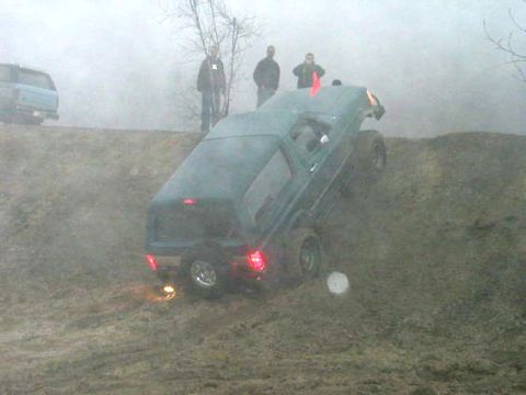1979 Ford Bronco - A dark green SUV navigates a steep, muddy incline with people watching.