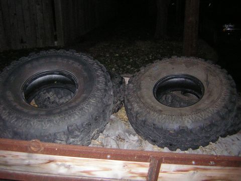 1995 Ford Bronco - Two mounted-off mud-terrain off-road tires with aggressive knobby tread standing side by side on a wooden surface at night. No wheels are f…