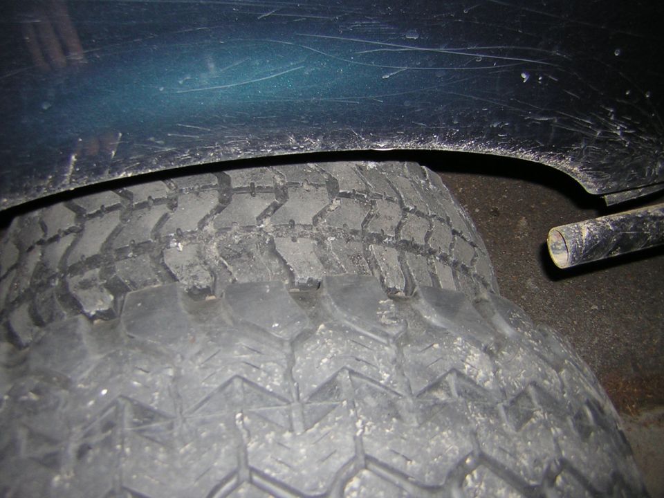 Dark green fender well above a worn tire, with a black exhaust pipe visible to the right