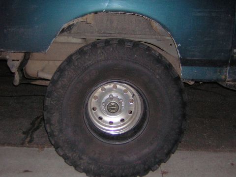 1995 Ford Bronco - Close-up of the rear wheel and fender of a teal SUV, revealing signs of wear and rust.