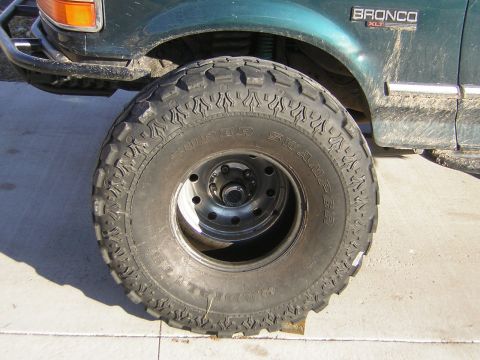 1995 Ford Bronco - A green Ford Bronco XLT with its front axle jacked up, and a large Super Swamper Radial mud tire on a black steel wheel leaning against the…