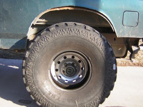 1995 Ford Bronco - Close-up of a Super Swamper Radial TSL mud tire mounted on a black slotted steel wheel under the rear fender of a teal Ford truck. The trim…
