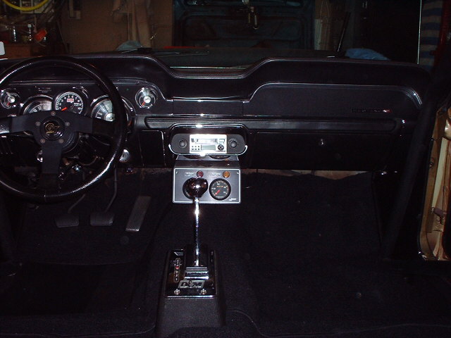 1967 Ford Mustang interior with black dashboard, aftermarket steering wheel, and floor shifter
