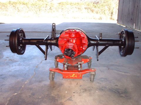 1967 Ford Mustang - A rear axle assembly, a bright red differential housing and black drum brakes, is shown mounted on a red wheeled stand.