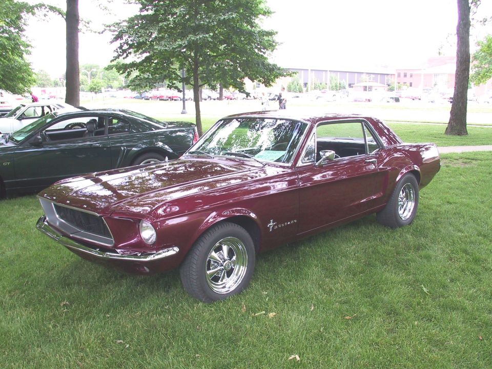 Dark maroon 1968 Ford Mustang coupe with chrome wheels parked on grass at a car show
