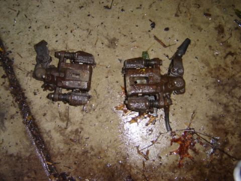 1992 Ford Bronco - Two brake calipers are shown on a wet, dirty floor with debris.