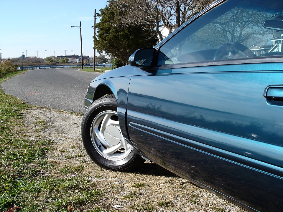 Front fender and alloy wheel of teal Ford Thunderbird parked on a roadside path