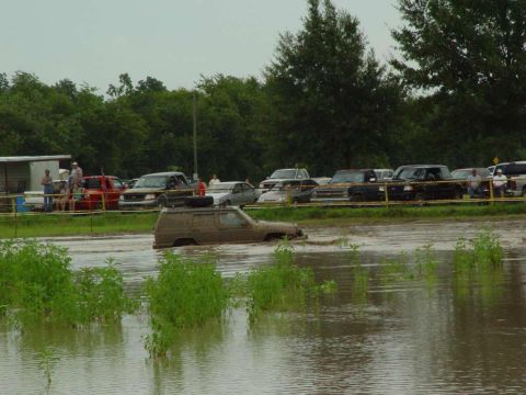 2000 Jeep Cherokee - A muddy SUV is stuck in flooded terrain, with spectators and other vehicles in the background.