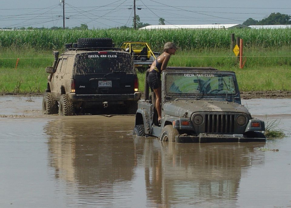 Muddy Jeep Cherokee towing a Jeep Wrangler stuck deep in a flooded mud pit at a Delta 4x4 Club event