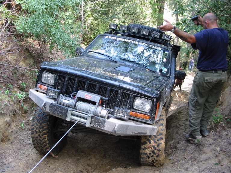 Black Jeep Cherokee XJ with roof light bar and winch on muddy trail